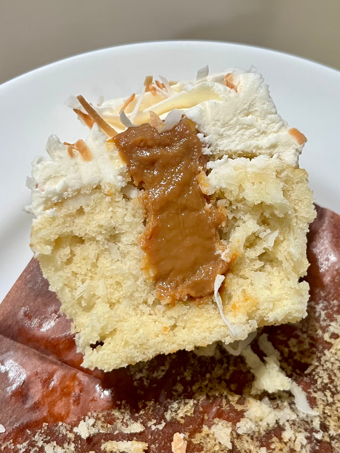 A Coconut Dulce de Leche cupcake cut in half on a white plate revealing the decadent Dulce de leche filled center.