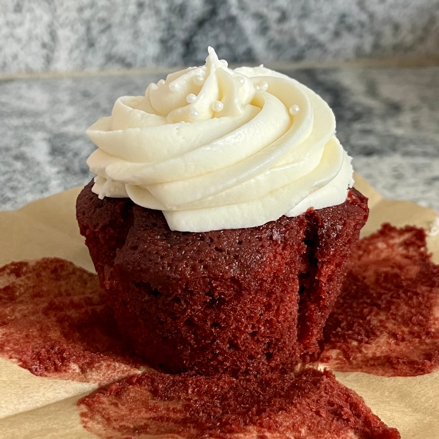 Image of an unwrapped Love At First Bite (red velvet) cupcake sitting on the wrapper. Lucious!