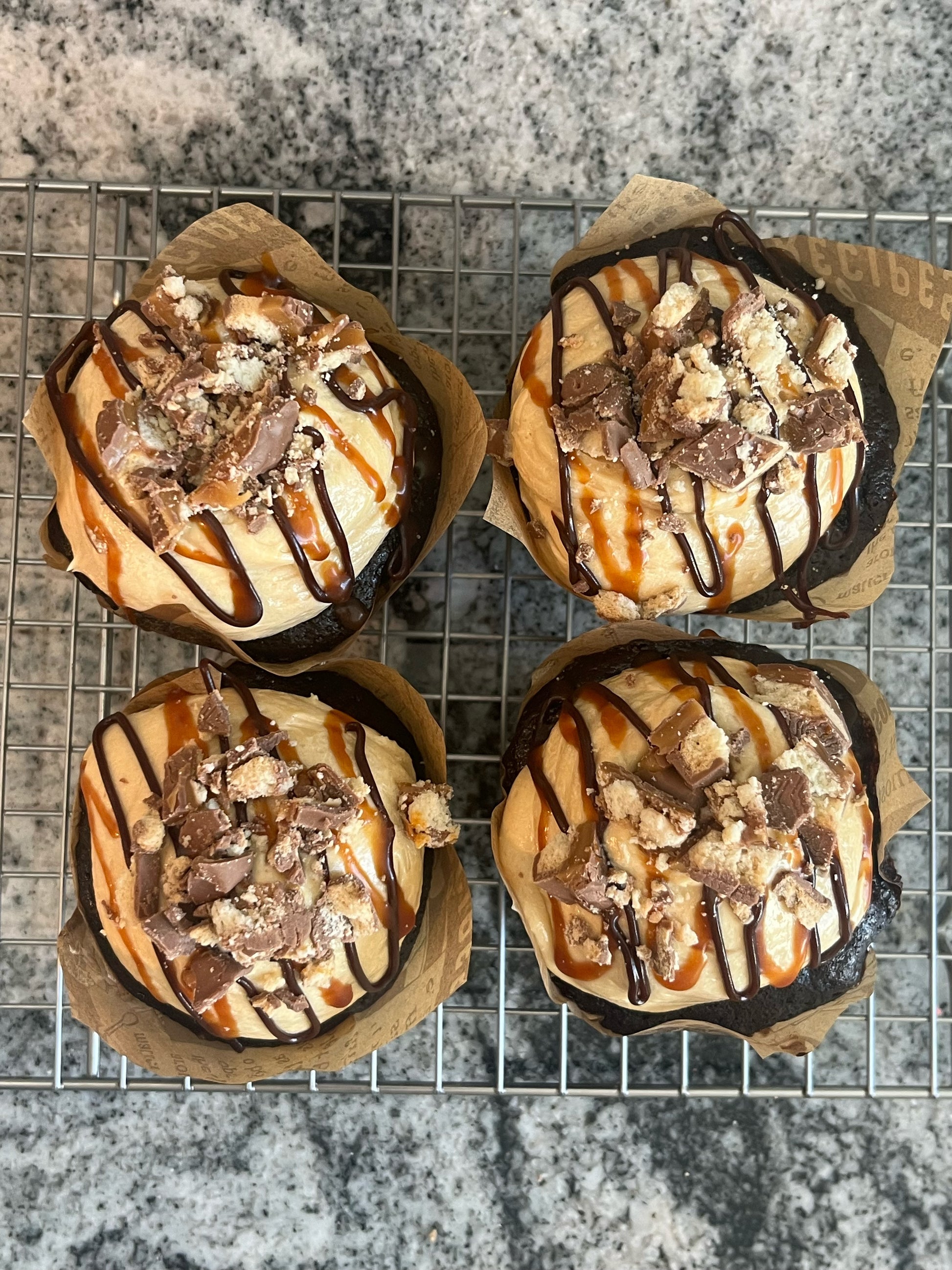 Overhead view of Four Chocolate Salted Caramel cupcakes covered in chocolate and salted caramel drizzle, topped with Twix candy crumble.