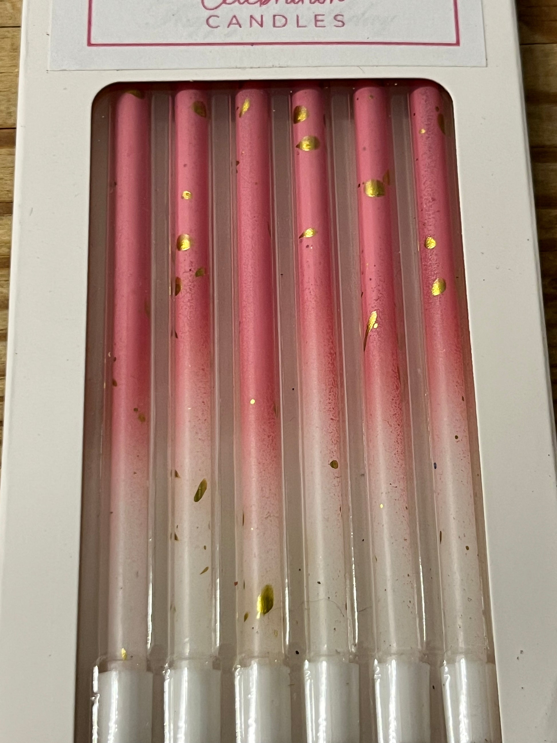 A close up of a box of six 4.7" tall skinny gradient white and pink candles with gold flecks.  The bottom of the candle is white and changes to pink about 1" from the bottom.  The candles are elegant and petite, yet tall and lovely.