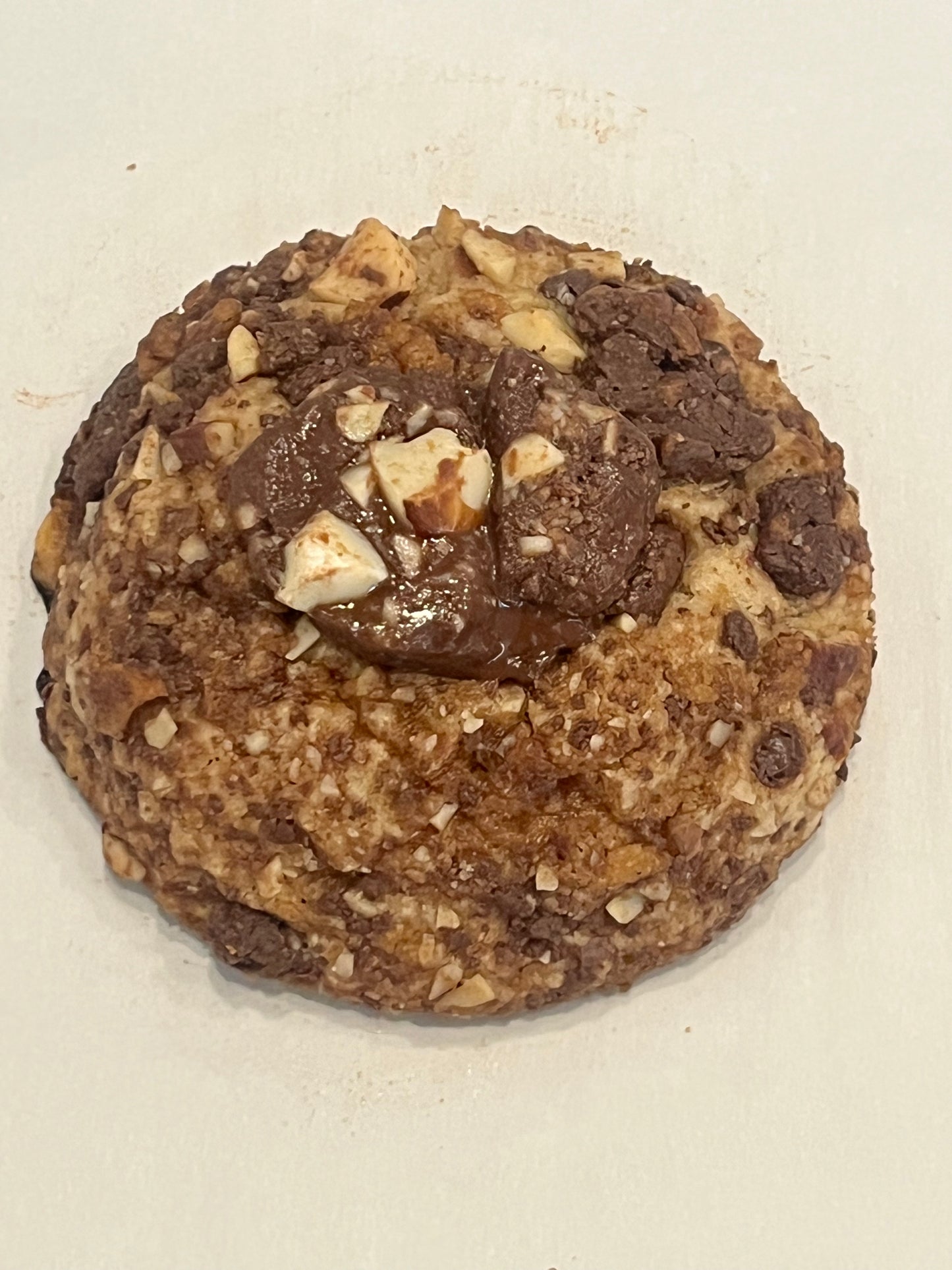 A close up of a Get Ur Toffee On cookie with almonds and a big chunk of melty chocolate on top.