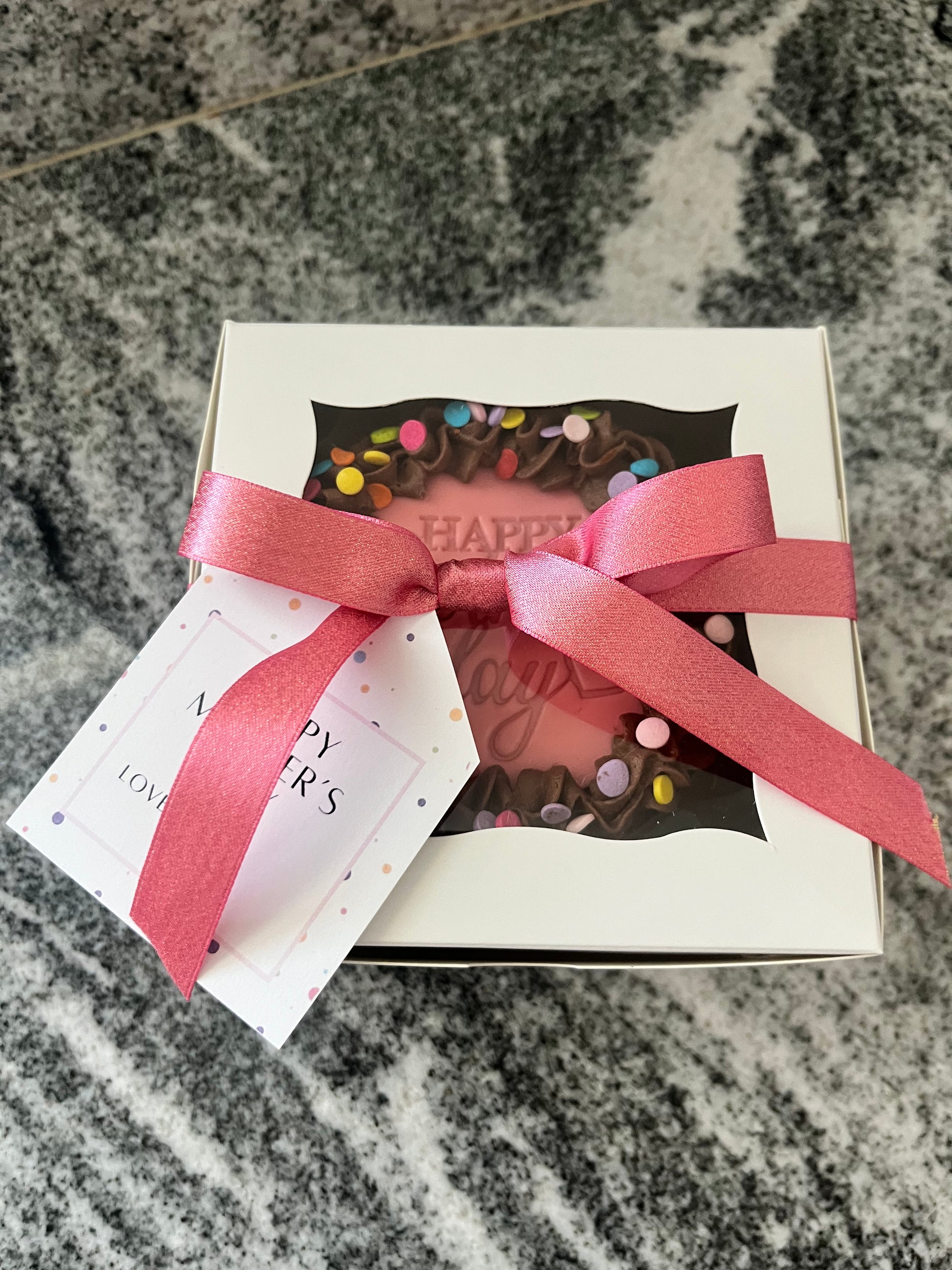 A chocolate mini cake packaged in a white box with pink ribbon and a hang tag, ready to go to its new home.