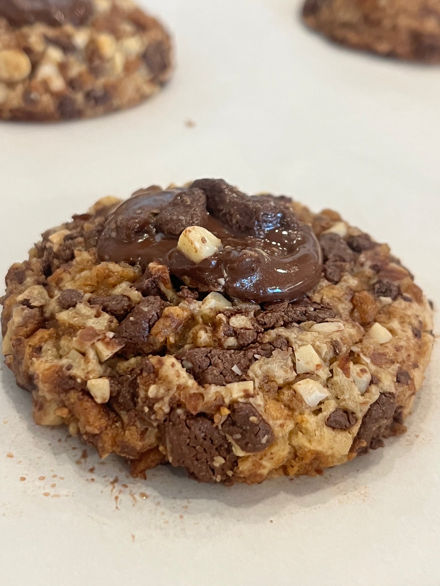 A close up of a Get Ur Toffee On cookie with almonds and a big chunk of melty chocolate on top.
