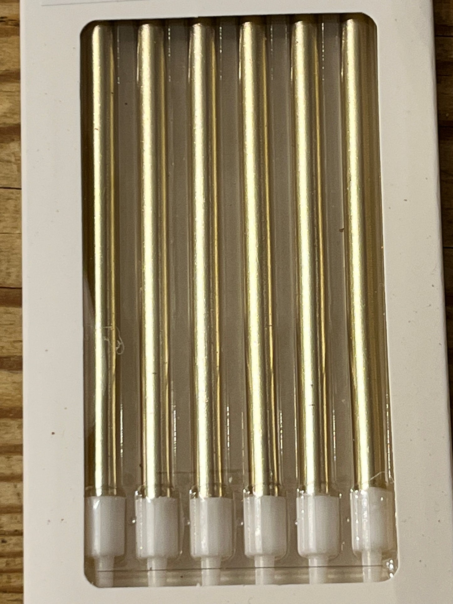 A coser look at a box of 6 shiny gold, skinny 4.7" tall candles. 