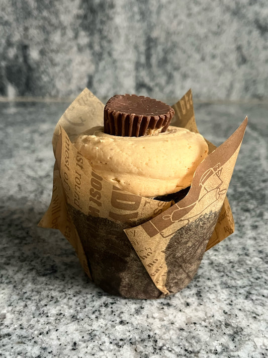 Side view of A decadent chocolate cupcake with a thick pile of peanut butter frosting and a peanut butter cup. 