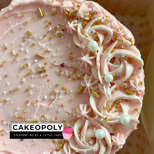 The most beautiful and tasty pink frosted cake with white pearls and gold sprinkles, featuring Cakeopoly branding.