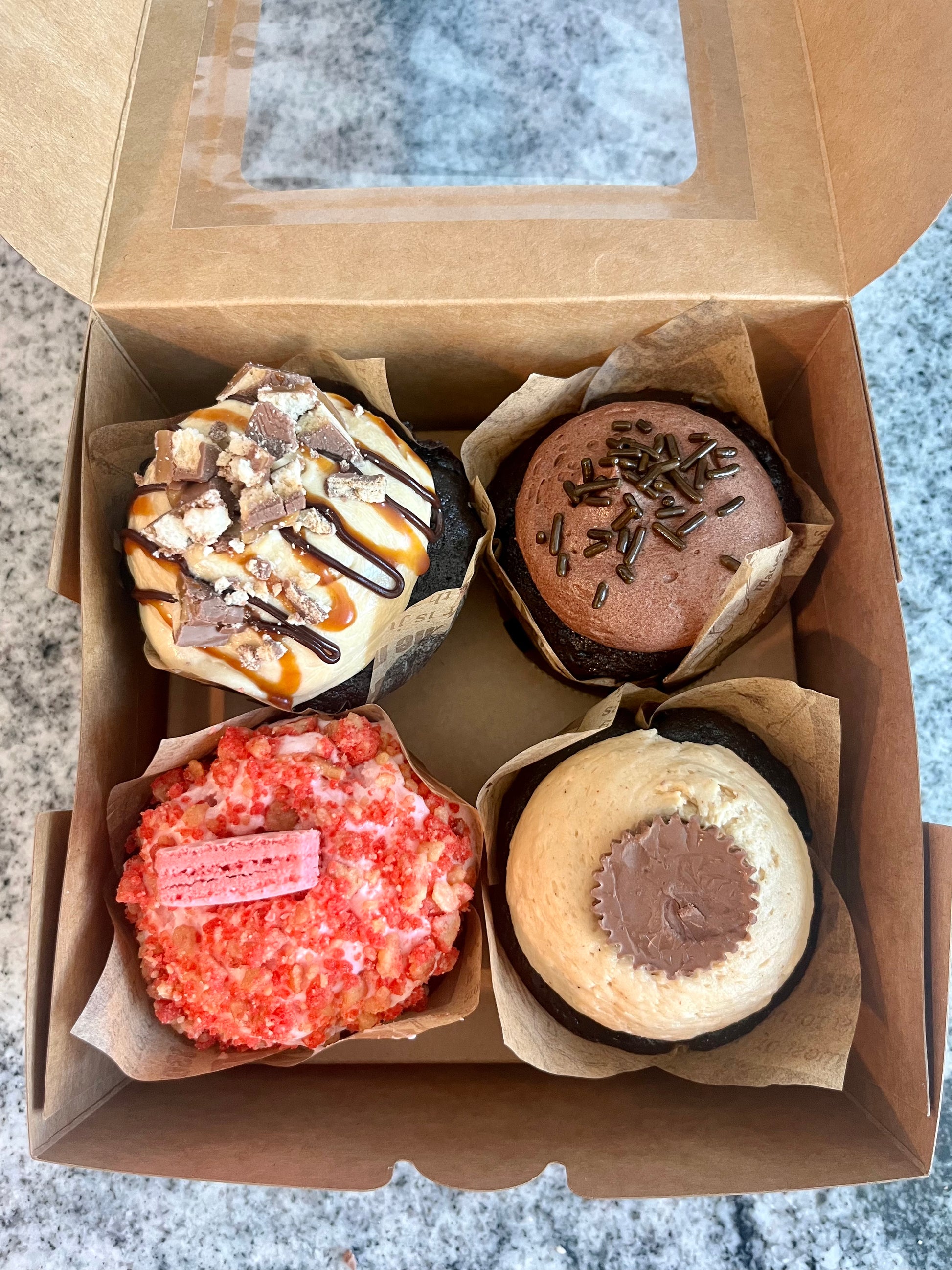 Chocolate Salted Caramel cupcake in a bakery box with three other cupcakes (Strawberry Shorty, Chocoholic and Big Pimpin' cupcakes).