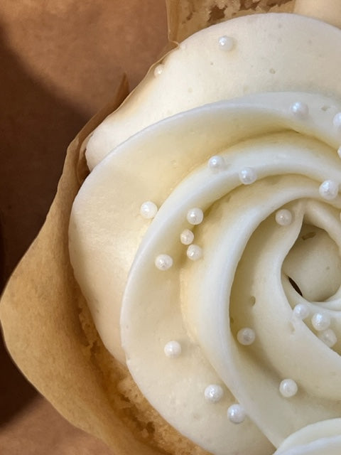 A close up from above of the gorgeous white ripples of frosting with pearl white nonpareils on a Very Vanilla cupcake.