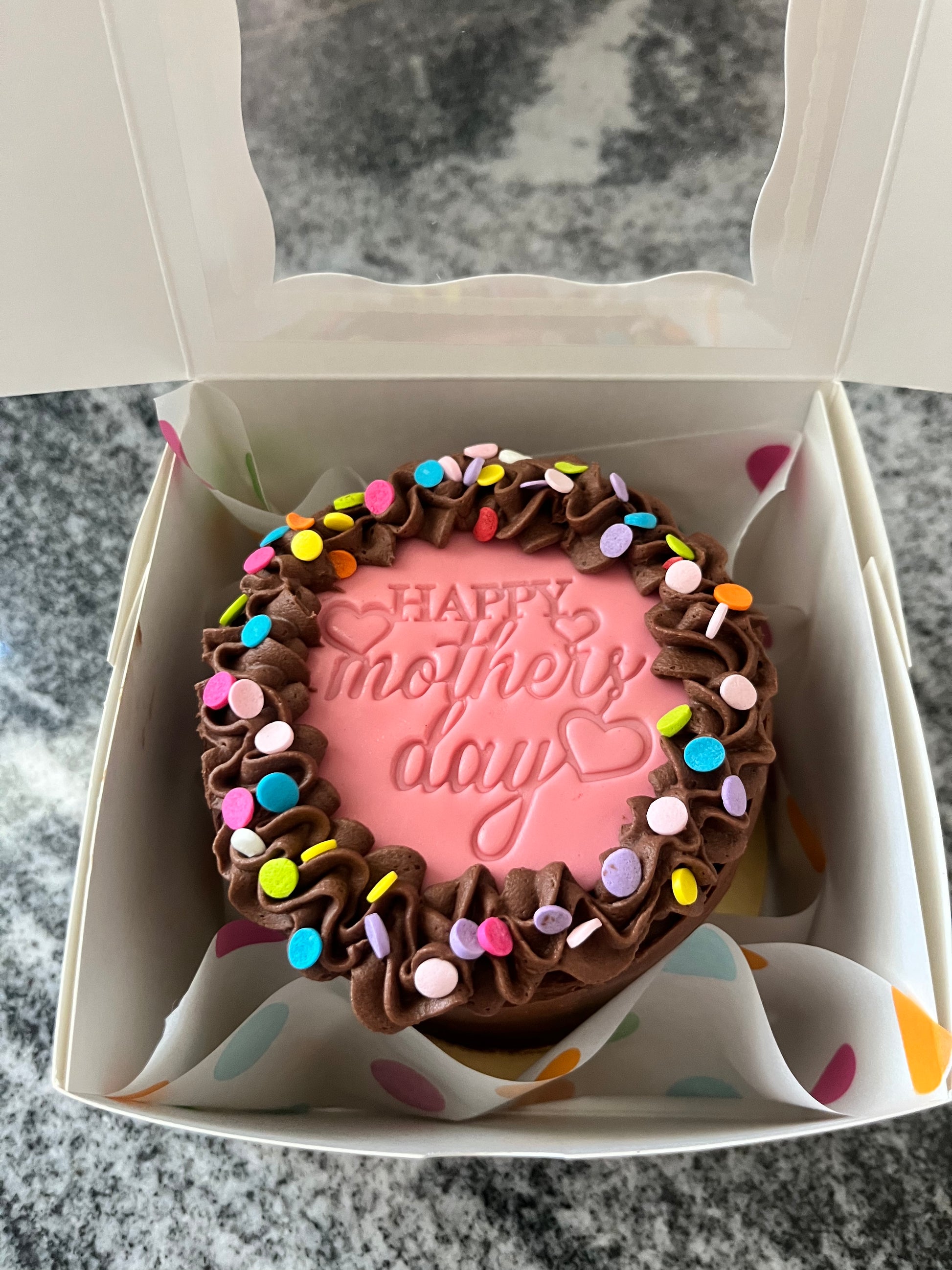 A chocolate mini cake sitting in a white box with polka dot paper, ready to go to its new home.