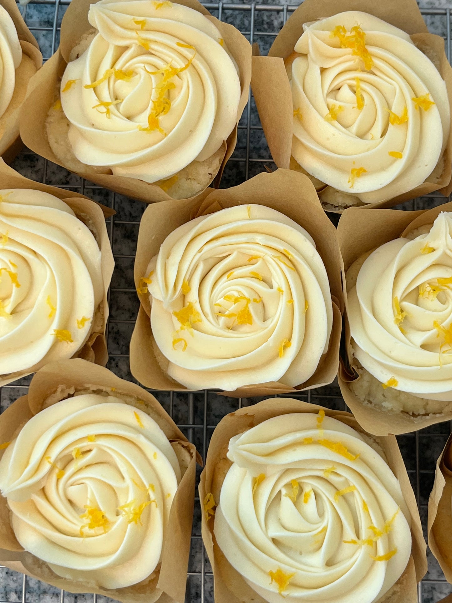 Seven Pucker Up! Cupcakes topped with fresh lemon zest on a bakers rack.