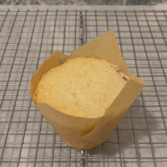 A vanilla cupcake in a light brown tulip wrapper sits atop a baking rack.  A gorgeous, rippled swirl of frosting is then piped onto a vanilla cupcake and tiny pearl white nonpareils are sprinkled on top.
